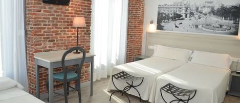 A hotel room with a brick wall, a desk with a chair, two beds, and a large framed picture on the wall.