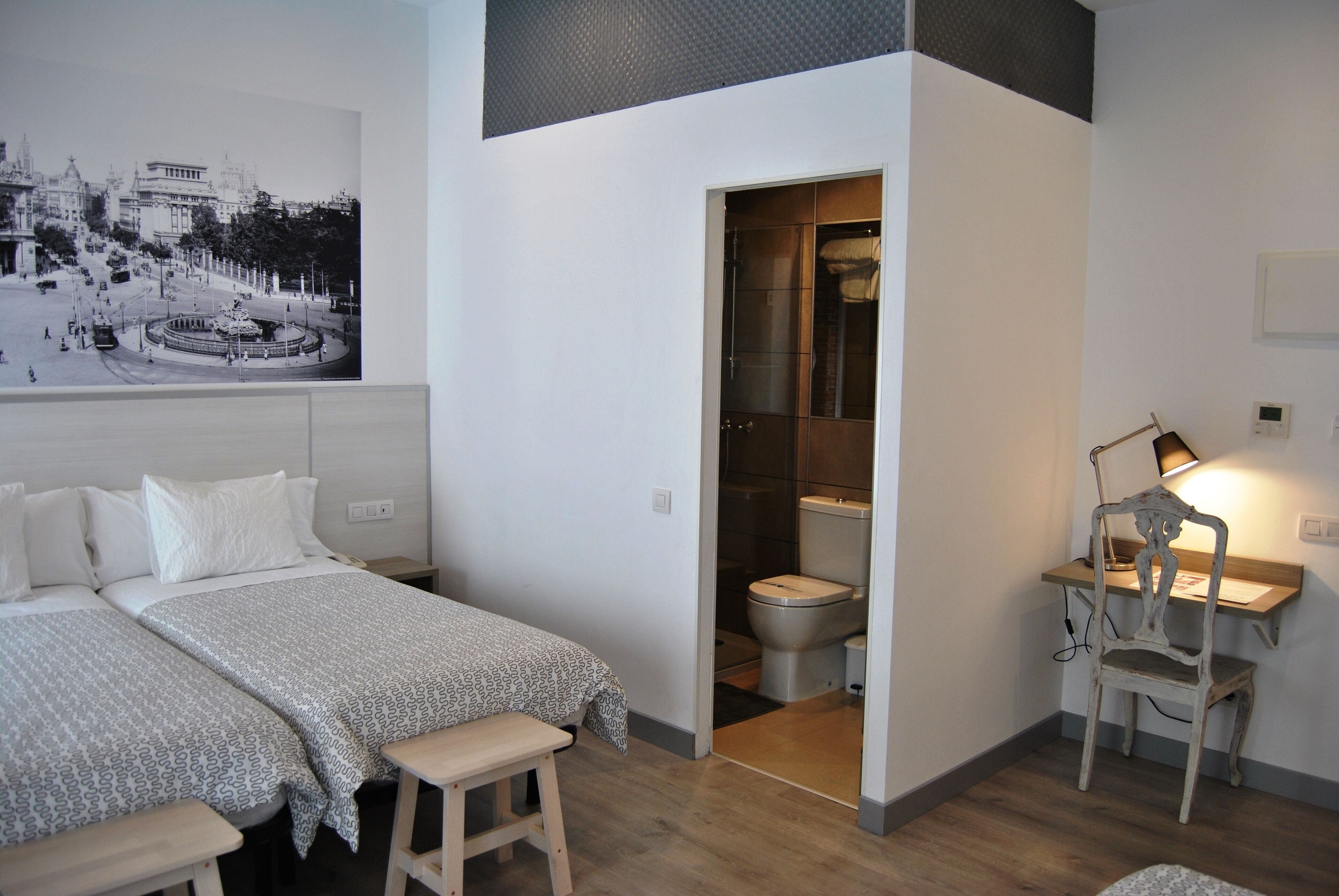 Une chambre avec deux lits, un bureau avec une chaise, et une salle de bain visible à travers une porte ouverte.