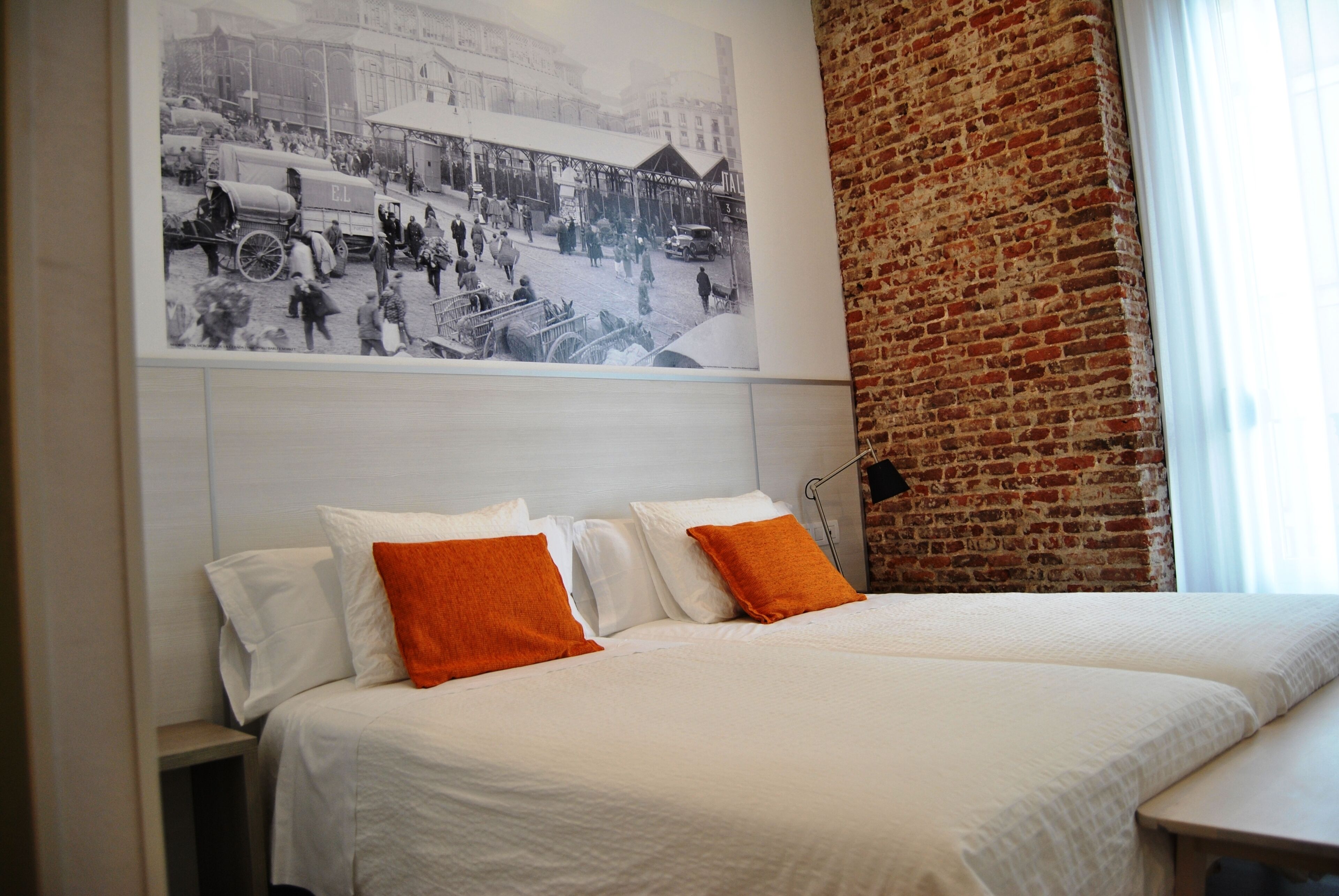 Une chambre d’hôtel avec un grand lit, deux oreillers, une tête de lit et un tableau représentant une scène de rue d’époque, accroché au mur.