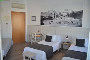 Ein Hotelzimmer mit zwei Betten, einem Schreibtisch, einem Stuhl, einem kleinen Tisch und einer Wand-Klimaanlage.