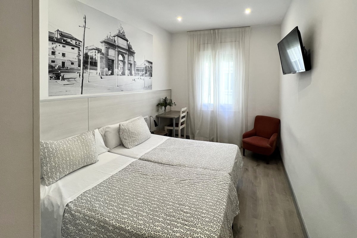 Ein Hotelzimmer mit einem großen Bett, einem Schreibtisch, einem Sessel, einem Fernseher und einem Fenster mit Vorhängen.
