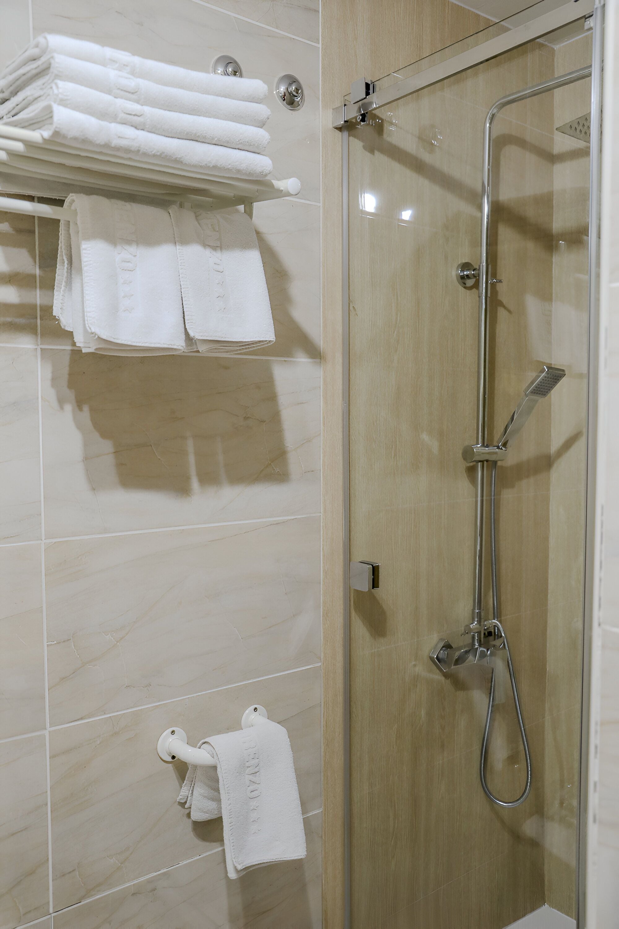 A shower area with a glass door, a towel rack with folded towels, and a shower head.