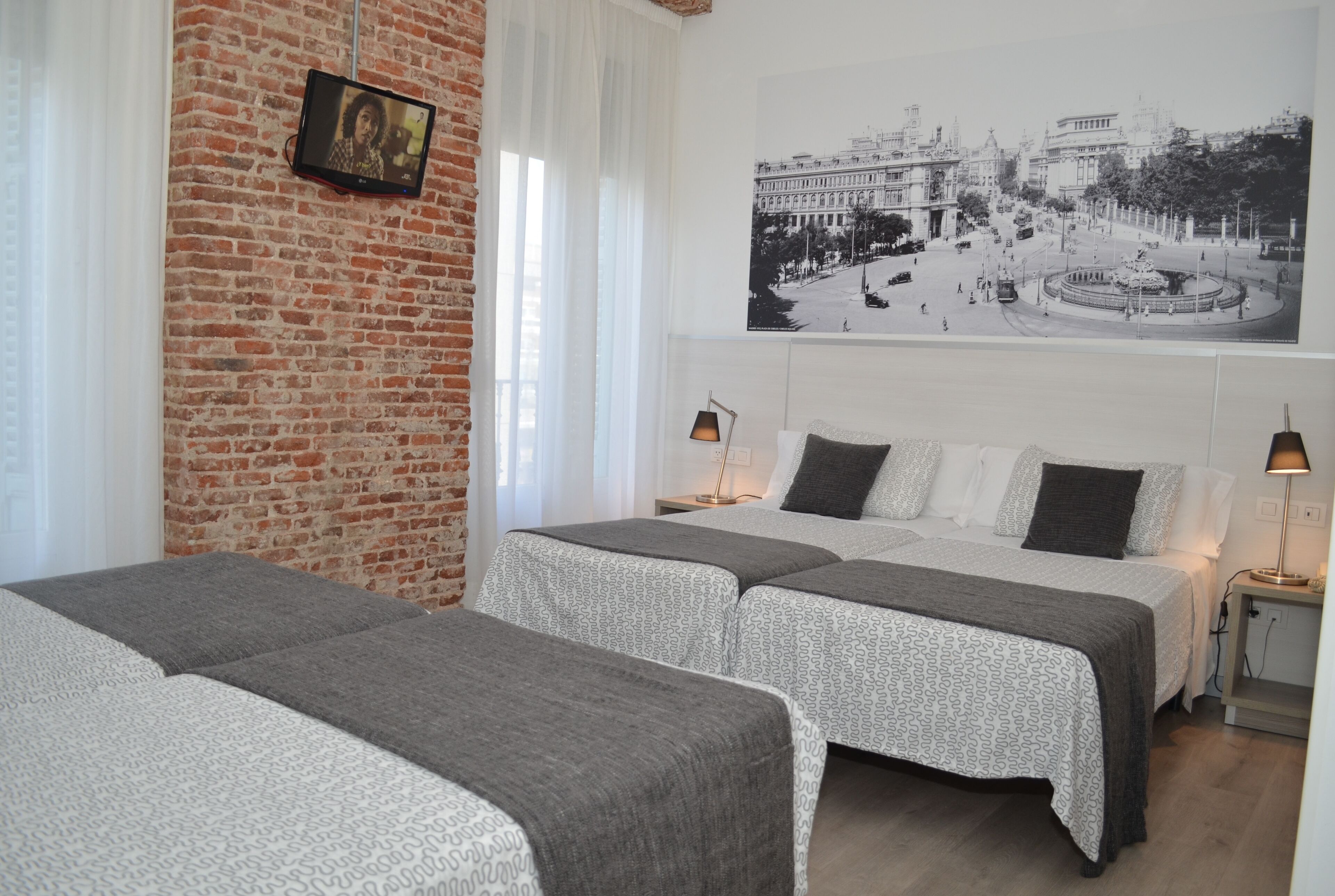 A hotel room with two beds, a brick wall, a large black and white photo, and a small table with a lamp.