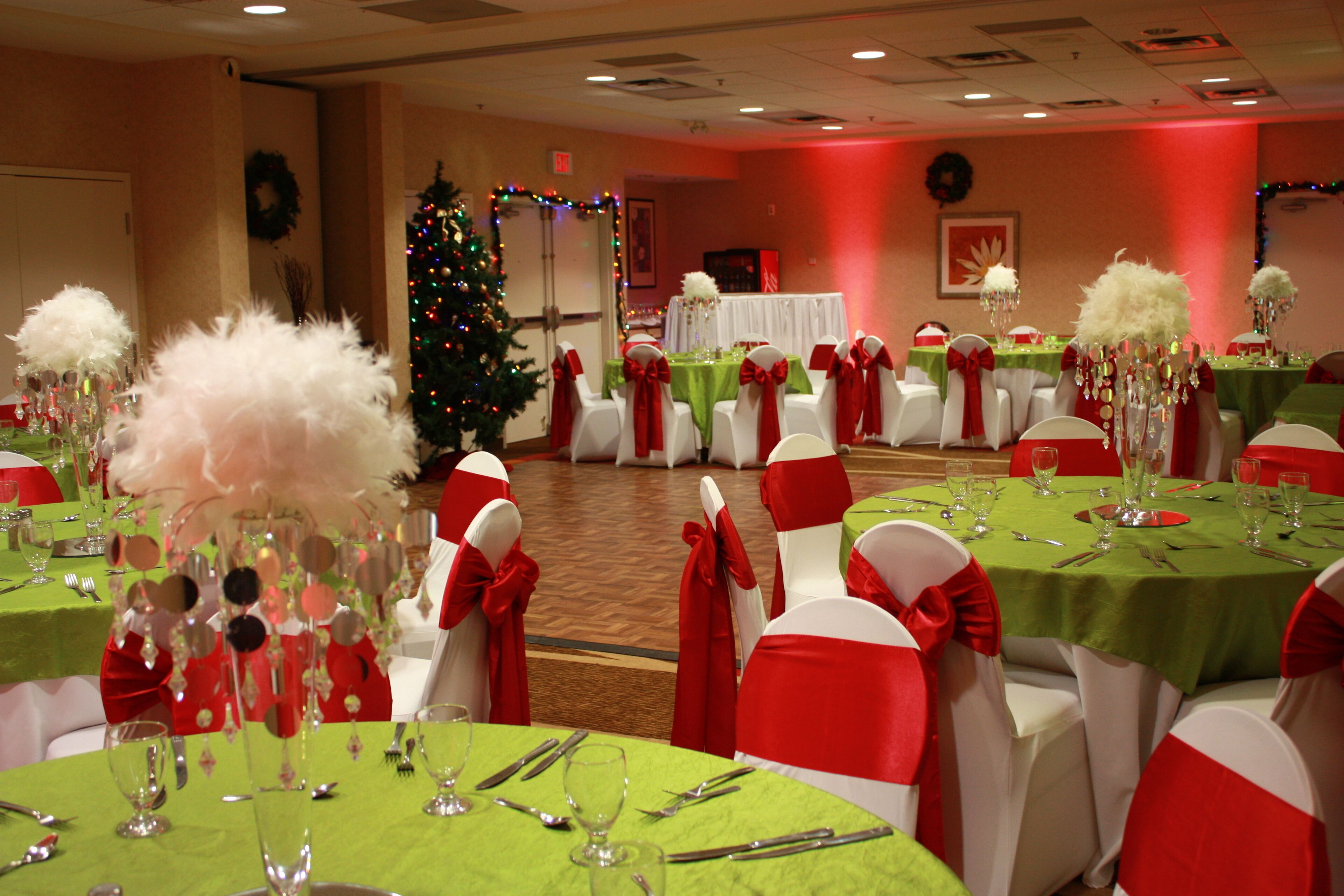A banquet hall with tables set for a formal event, decorated with red and white chairs and green tablecloths.