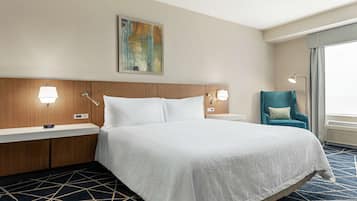 Ein Hotelzimmer mit einem großen Bett, einem Holz-Kopfteil, zwei Nachttischen mit Lampen, einem blauen Sessel und einem Bild an der Wand.