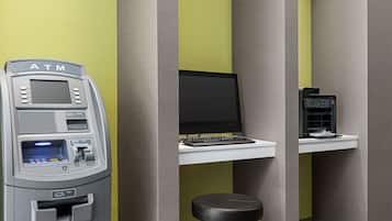 An ATM machine, a computer, and a coffee machine in a room with green and grey walls.