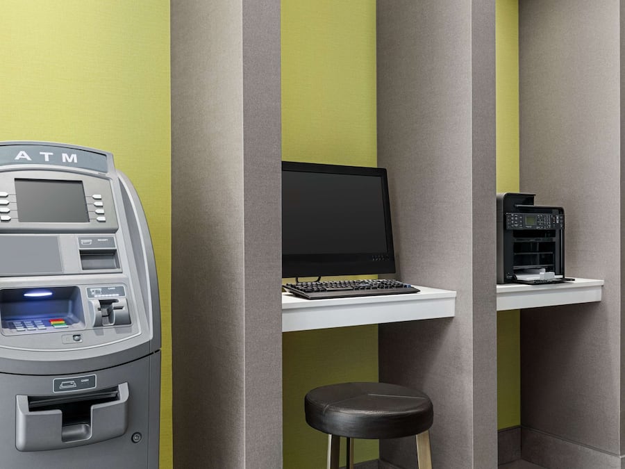 An ATM machine, a computer, and a coffee machine in a room with green and grey walls.