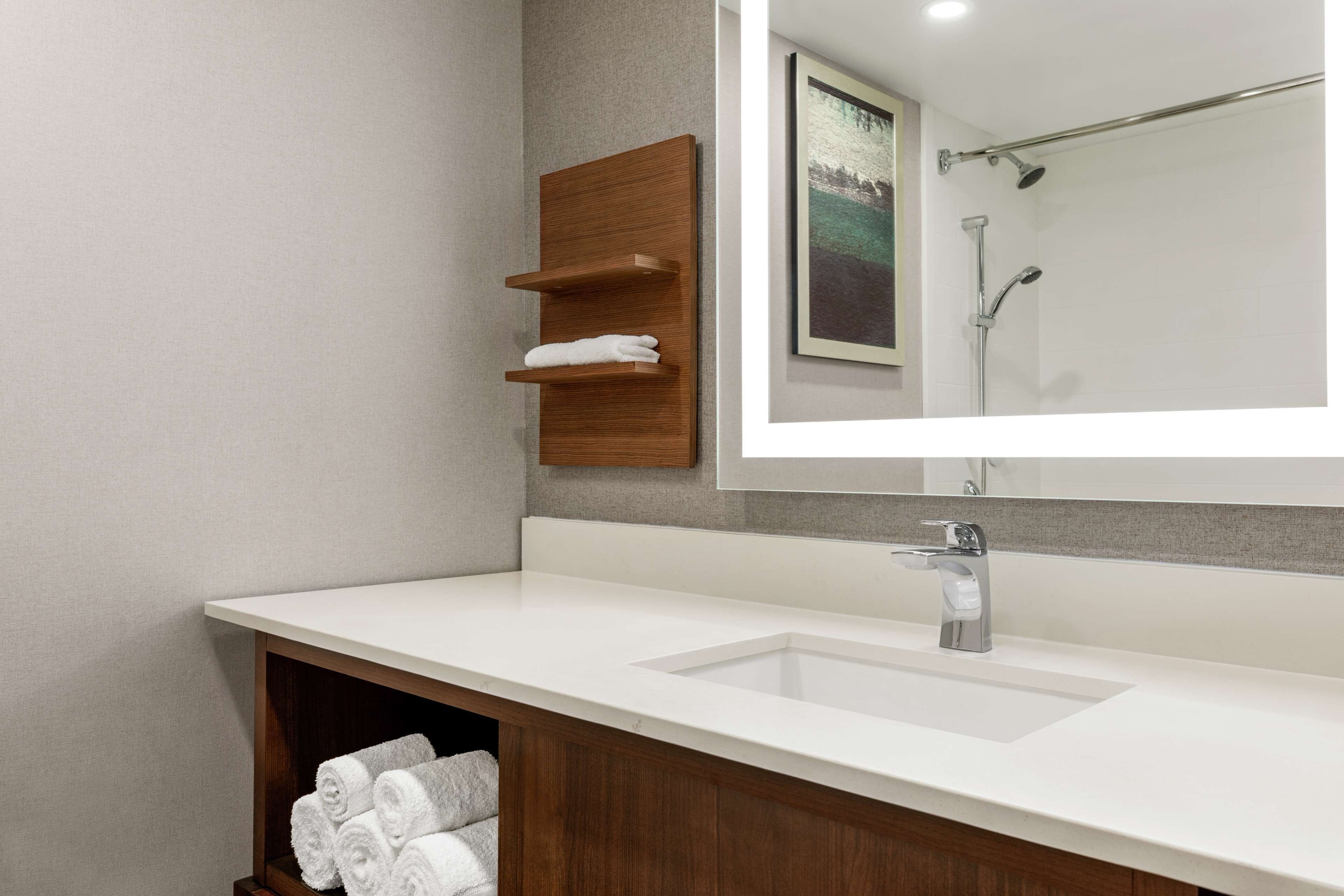 A modern bathroom with a white sink, wooden towel racks, and a large mirror reflecting a shower area.