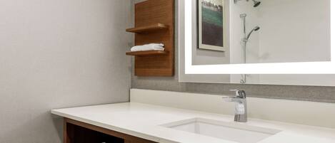 A modern bathroom with a white sink, wooden towel racks, and a large mirror reflecting a shower area.