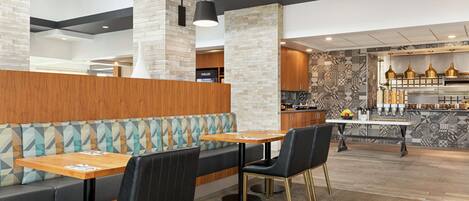 A modern restaurant with a wooden booth seating area, a central dining table, and a patterned backsplash in the kitchen area.