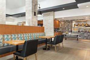 A modern restaurant with a wooden booth seating area, a central dining table, and a patterned backsplash in the kitchen area. - Hilton Garden Inn Kitchener/Cambridge (Cambridge)