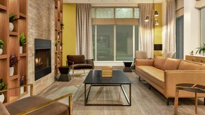 A modern living room with a fireplace, leather sofa, and wooden shelves with plants. - Hilton Garden Inn Kitchener/Cambridge (Cambridge)