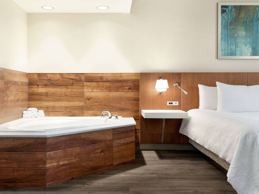 Een moderne badkamer met een houten wastafelmeubel, een vrijstaand bad, een witte wasbak en een nachtkastje met een lamp.