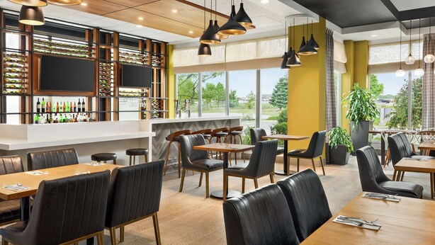 A modern restaurant with a bar area, multiple seating options, and large windows offering a view of the outdoors. - Hilton Garden Inn Kitchener/Cambridge (Cambridge)