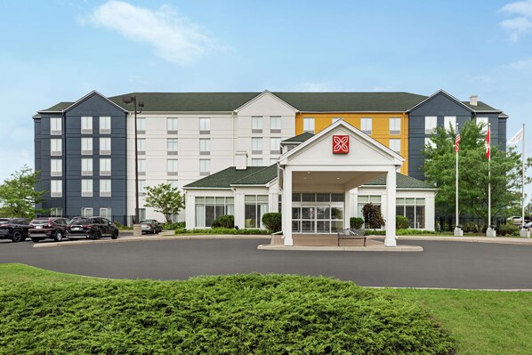 A multi-story hotel with a central entrance, parking lot, and flag display. - Hilton Garden Inn Kitchener/Cambridge (Cambridge)