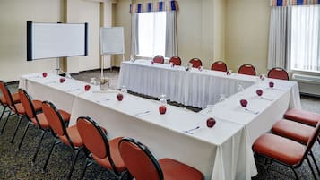 Ein Konferenzraum mit langem Tisch, Stühlen, einer Whiteboard-Tafel und einer Projektionsleinwand.