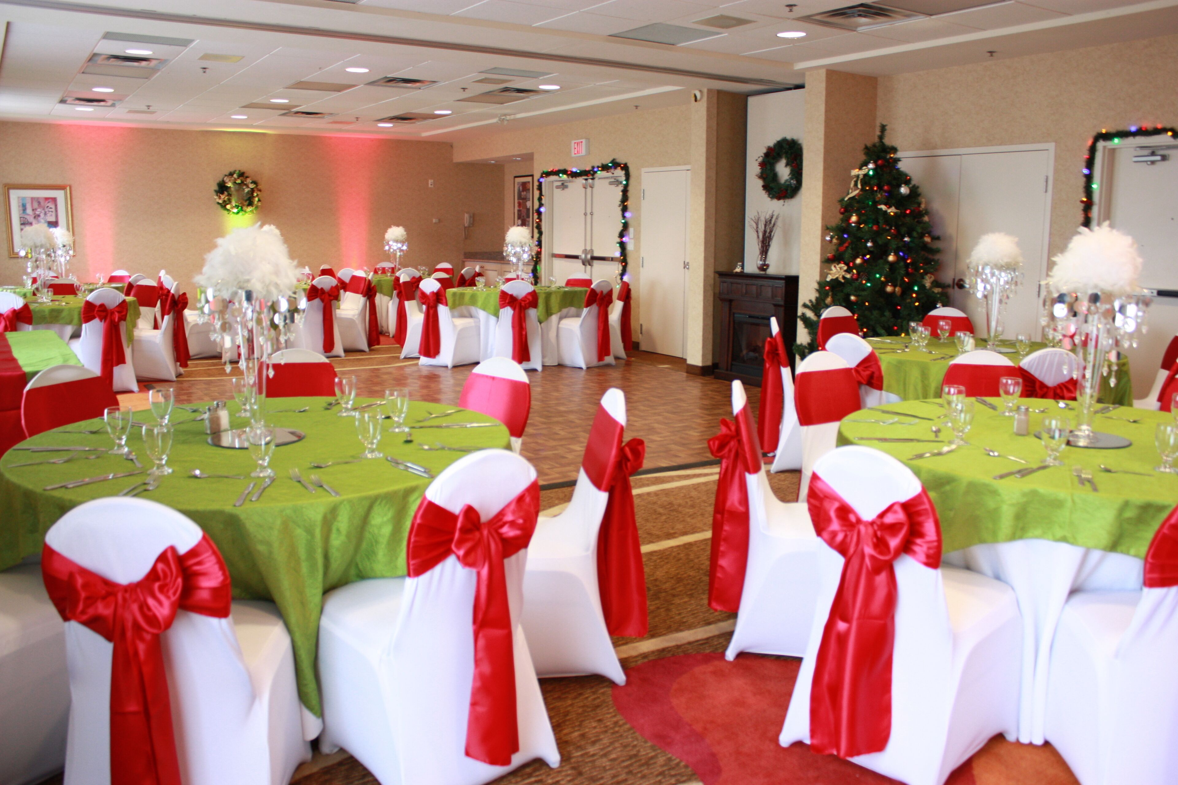 A banquet hall with round tables covered in green tablecloths and white chairs with red sashes.