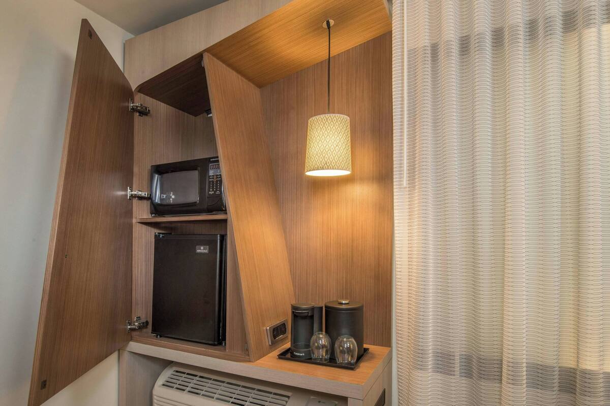 A compact kitchenette with a microwave, refrigerator, and coffee maker on a wooden countertop.