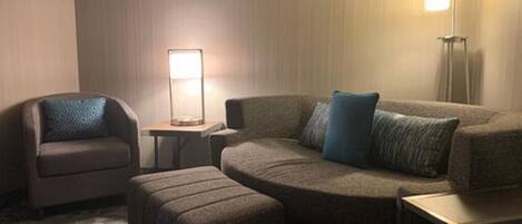 A hotel room with a sofa, a chair, a small table, and a floor lamp.