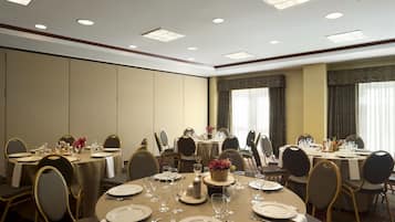Un salón de conferencias con mesas redondas dispuestas para comidas, equipado con sillas, platos, cubiertos y cristalería.