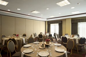 Un salón de conferencias con mesas redondas dispuestas para comidas, equipado con sillas, platos, cubiertos y cristalería.