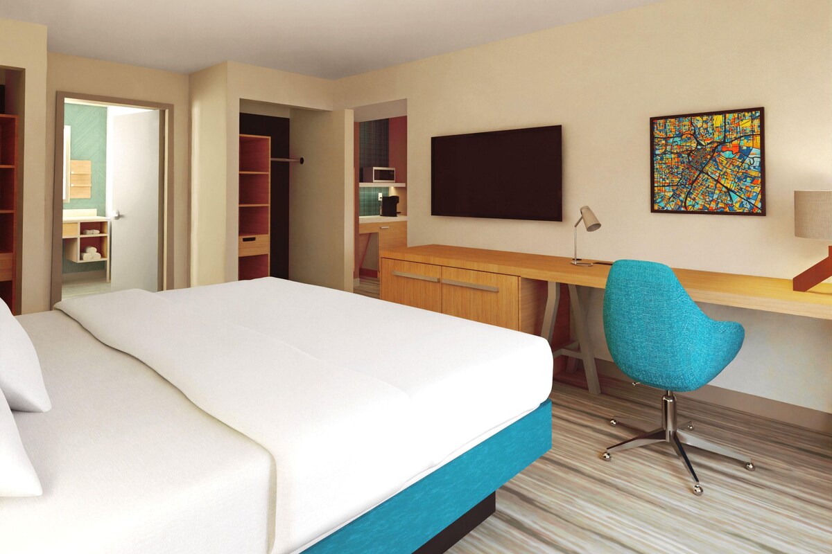 Habitación de hotel con cama, escritorio, silla, televisor y una obra de arte llamativa en la pared.