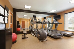 Un gimnasio con cintas de correr, elípticas, una pelota de ejercicios roja y un banco de pesas.