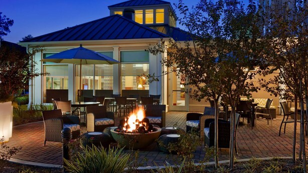 Un patio al aire libre con un hogar para fuego, asientos y un edificio con ventanas amplias y techo azul.