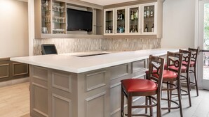 Una cocina con una isla grande, taburetes de bar y armarios empotrados con puertas de cristal.