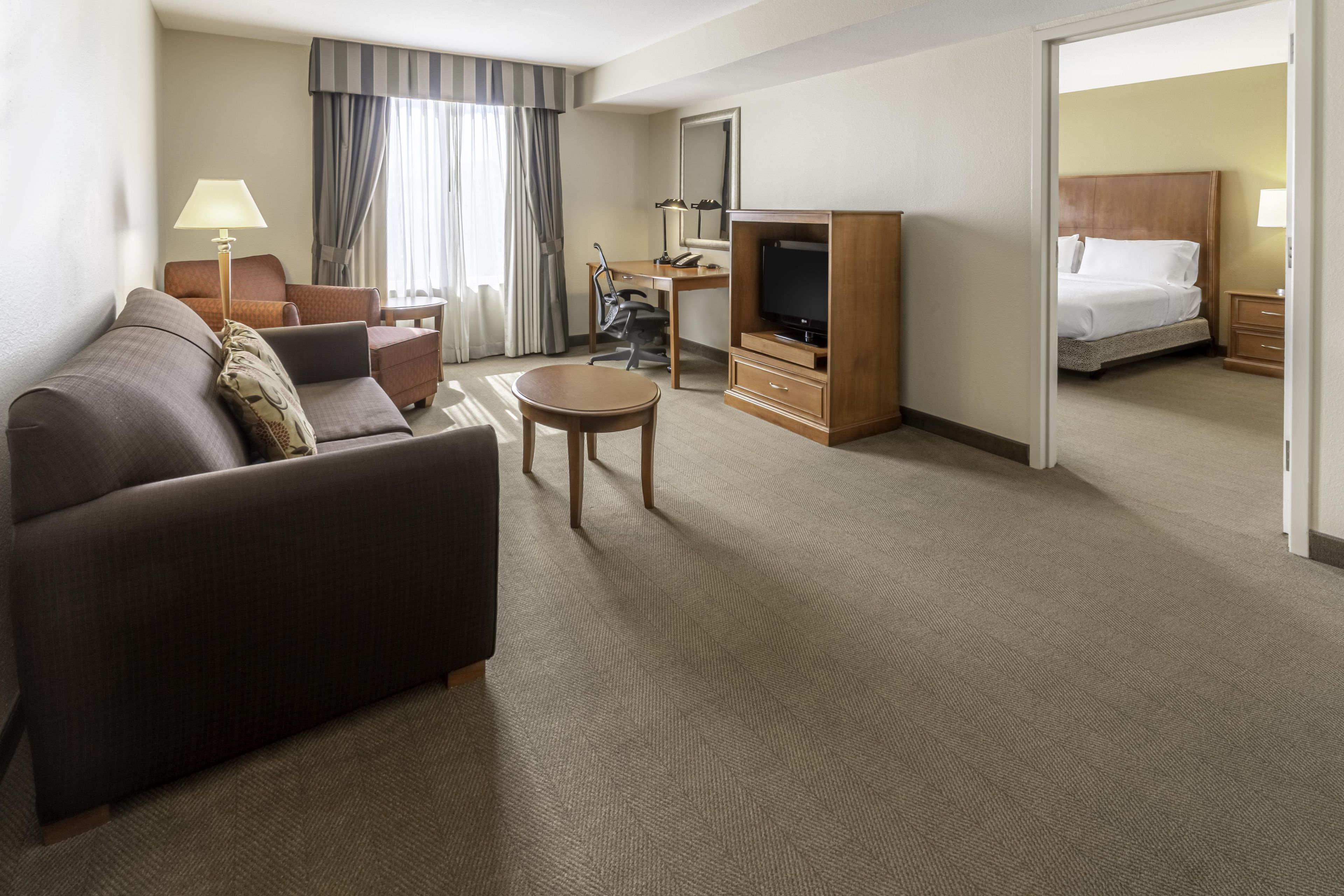 A hotel room with a sofa, a small table, a TV stand, a desk, and a bed.
