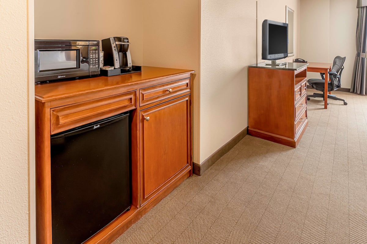 A hotel room with a wooden desk, a microwave, a coffee maker, a television, and a chair.