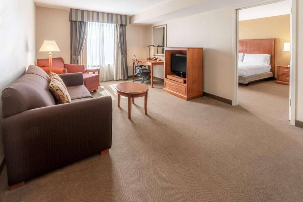 A hotel room with a sofa, a small table, a TV, a desk, and a bed.