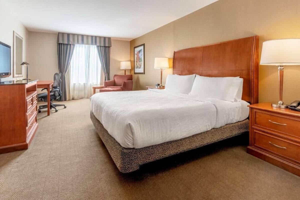 A hotel room with a large bed, a desk with a chair, a television, and a lamp.