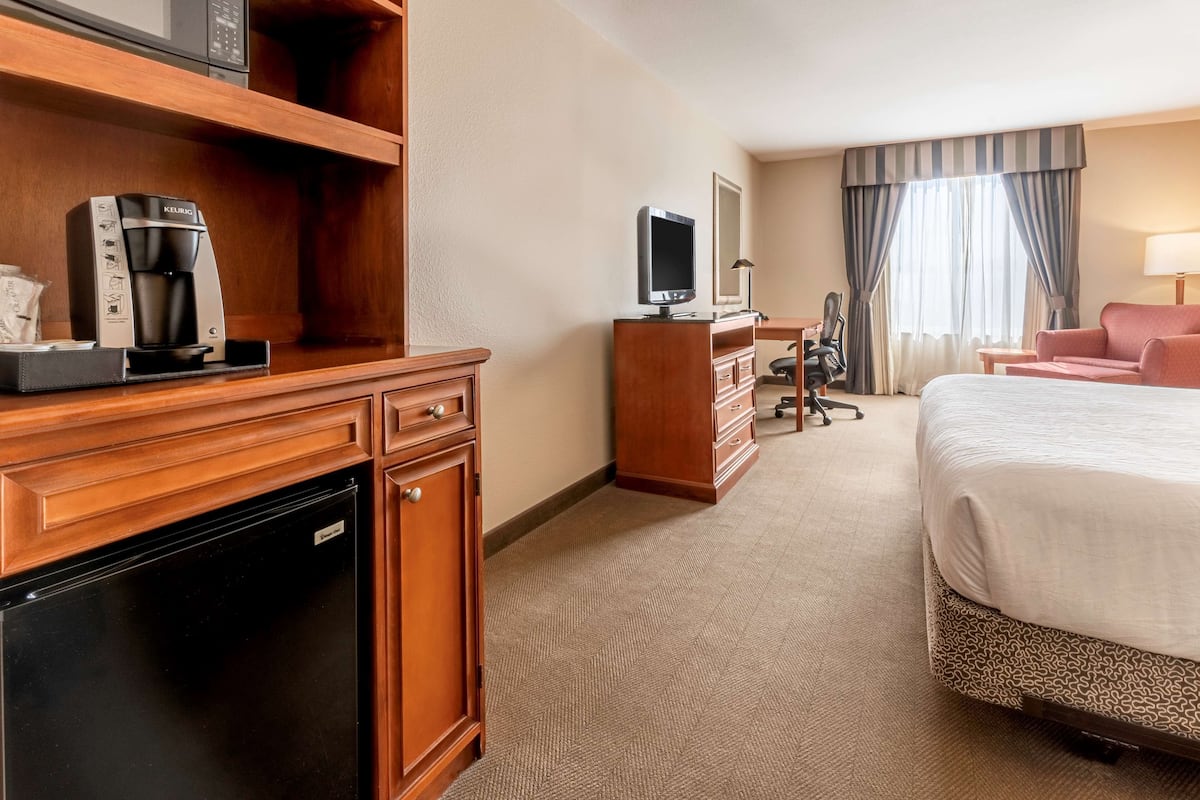 A hotel room with a bed, a desk with a computer, a coffee maker, and a television.