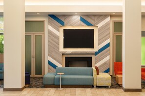 A modern lobby with a flat-screen TV mounted above a fireplace, a blue sofa, and a small round table.