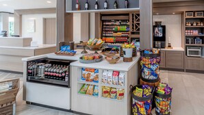 Zona de recepción de un hotel con una estación de bebidas, dispensadores de aperitivos y un televisor.