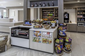 A snack bar with various packaged snacks, a refrigerator with beverages, and a display of bottled water. - Hilton Garden Inn Houston/The Woodlands (The Woodlands)
