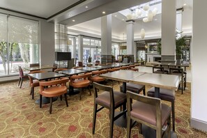 A spacious dining area with multiple tables and chairs, large windows, and a fireplace. - Hilton Garden Inn Houston/The Woodlands (The Woodlands)