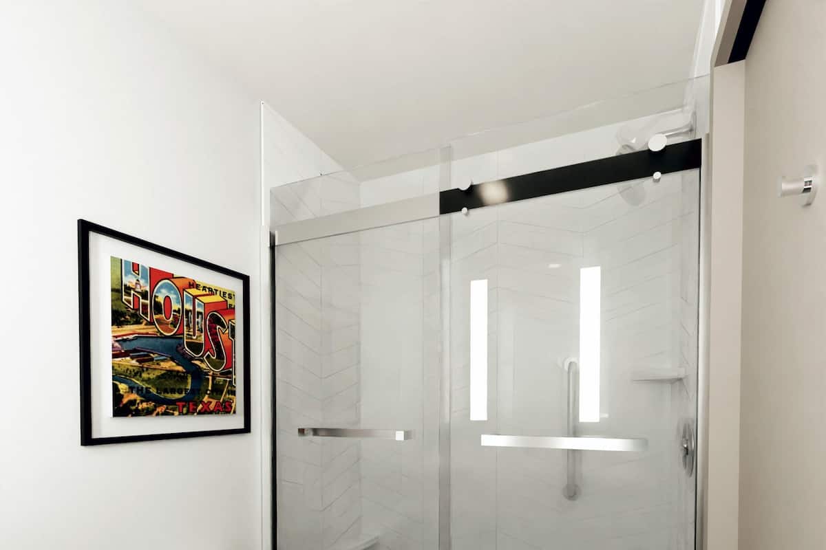 A modern bathroom with a glass shower enclosure, a toilet, and a framed picture on the wall.