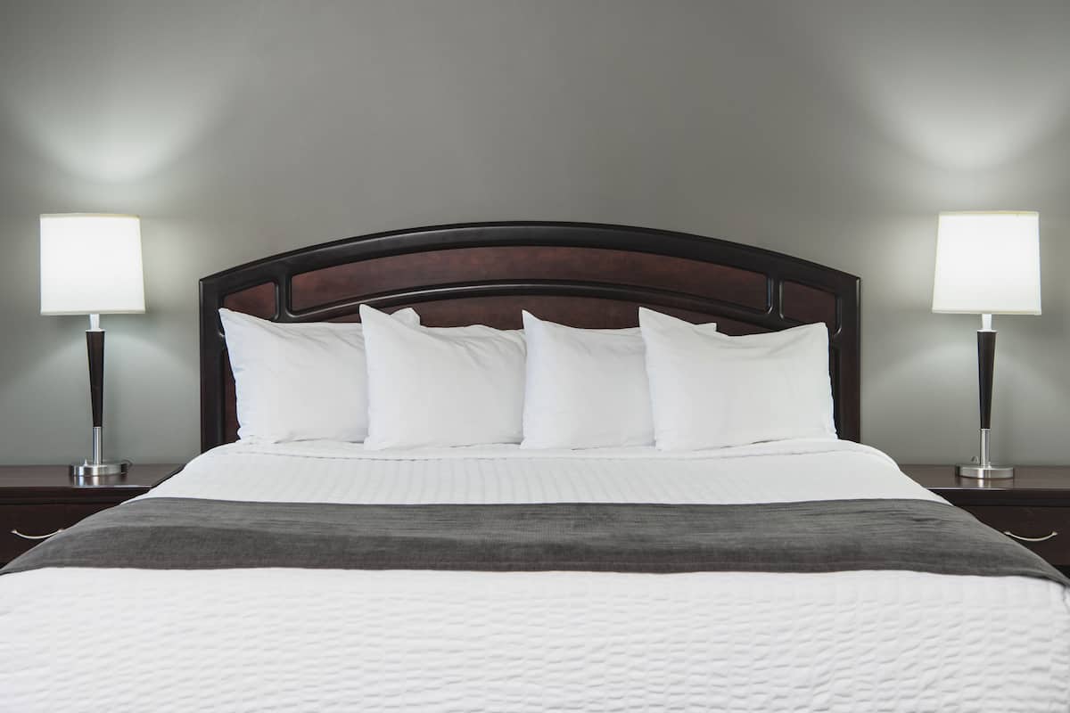 A neatly made bed with a dark headboard, white bedding, and a gray throw blanket. There are two bedside lamps on either side of the bed.