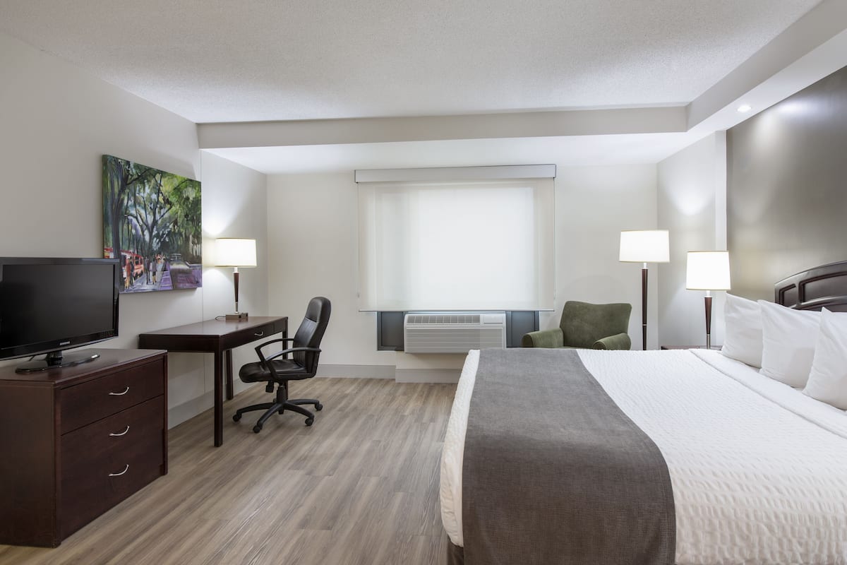 A hotel room with a bed, desk, chair, TV, and two lamps.