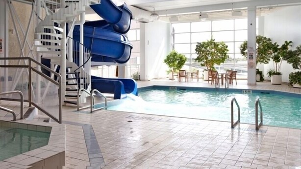 Une piscine intérieure dotée d’un toboggan, d’un escalier et d’un espace détente avec des tables et des chaises.
