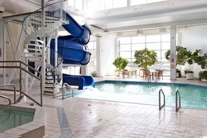 Une piscine intérieure dotée d’un toboggan, d’un escalier et d’un espace détente avec des tables et des chaises.