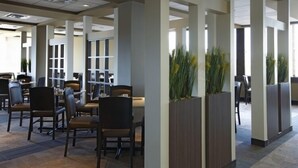 Un espace intérieur moderne doté d’un espace central ouvert, entouré de hautes colonnes, et comprenant des tables et des chaises pour les repas ou les réunions.