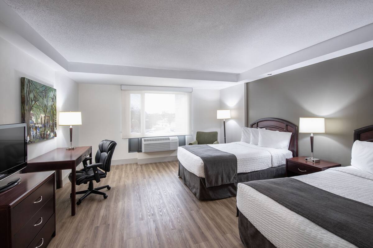 A hotel room with two beds, a desk, a chair, a TV, and a window with blinds.