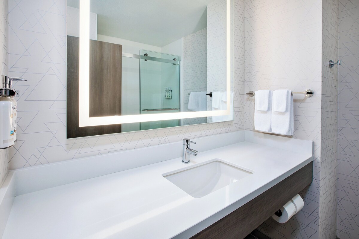 A modern bathroom with a large mirror, a white sink, and a glass shower enclosure.