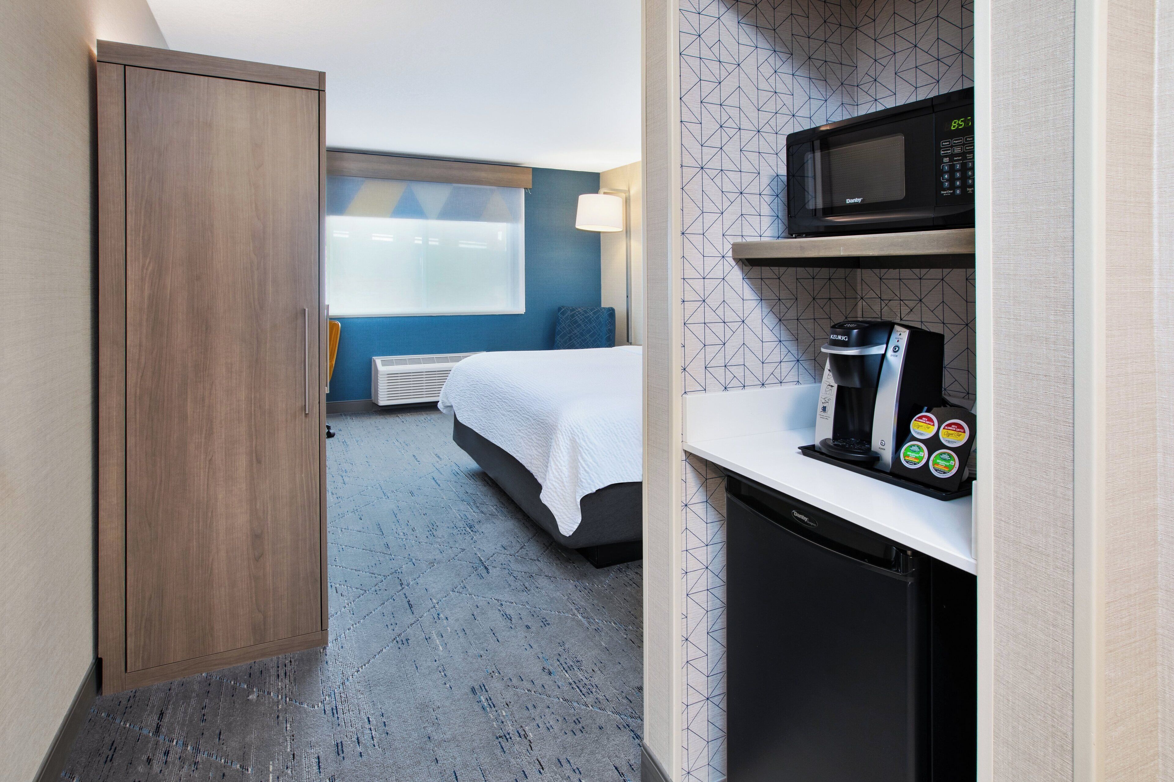 Habitación de hotel con cama, armario, microondas, cafetera y lavavajillas.