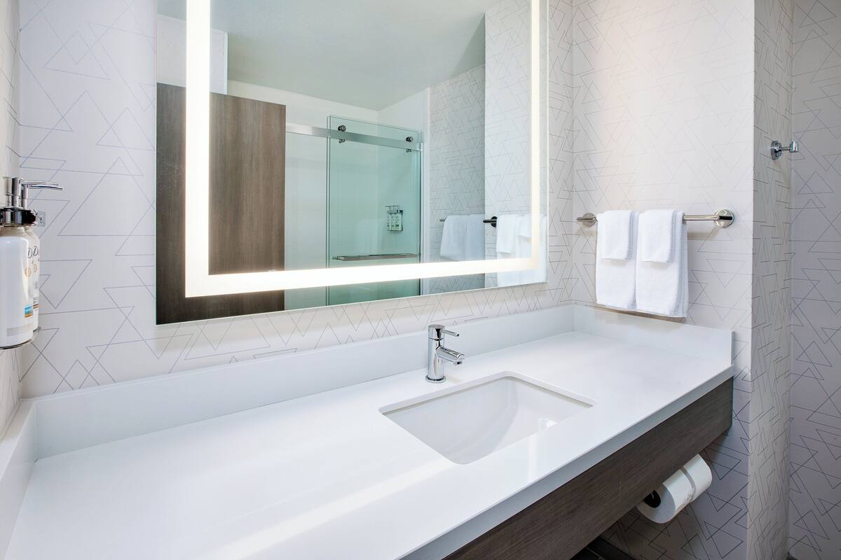 A modern bathroom with a large mirror, a white sink, and a glass shower enclosure.