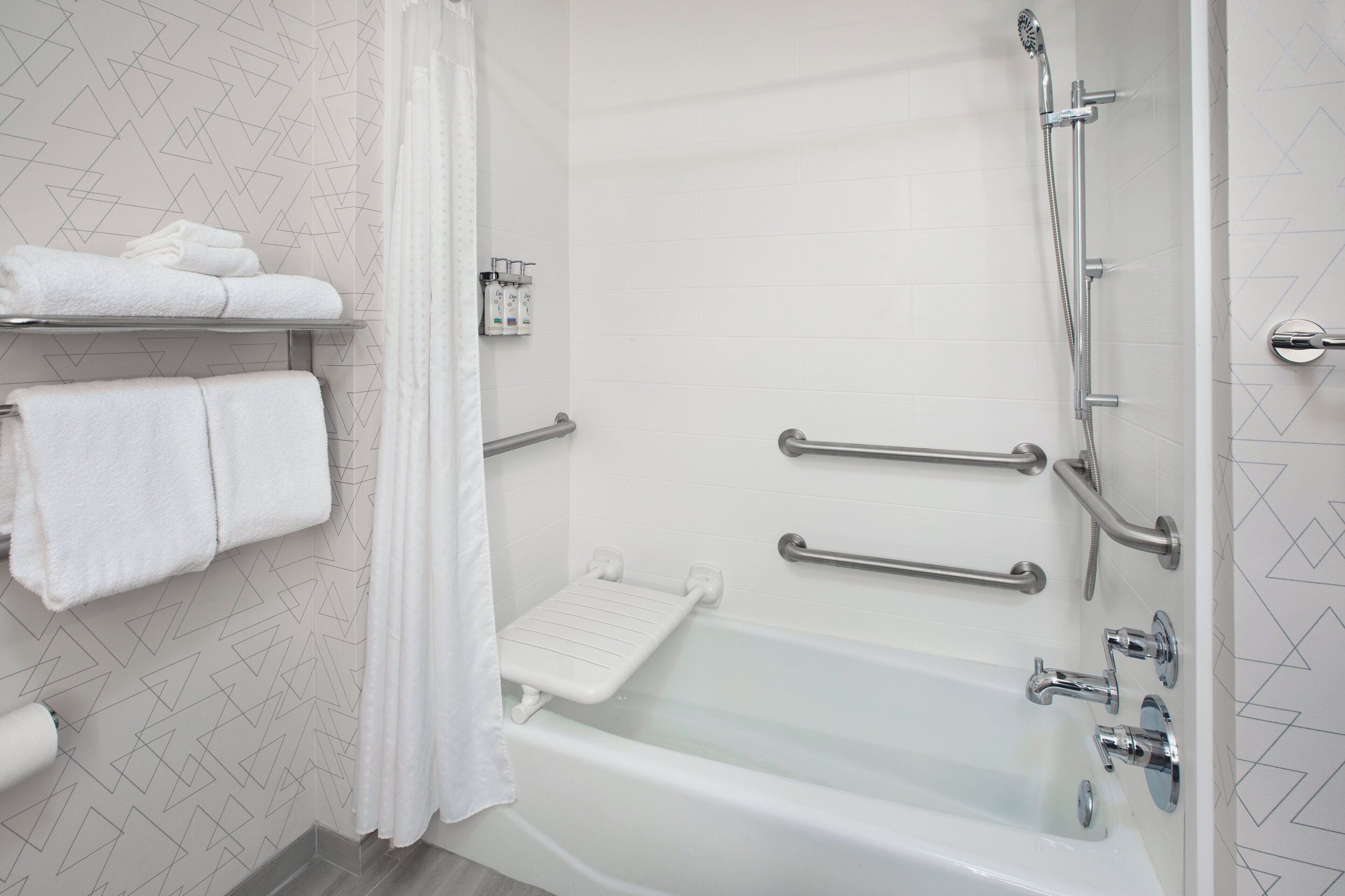 A modern bathroom with a bathtub, handrails, and a showerhead.