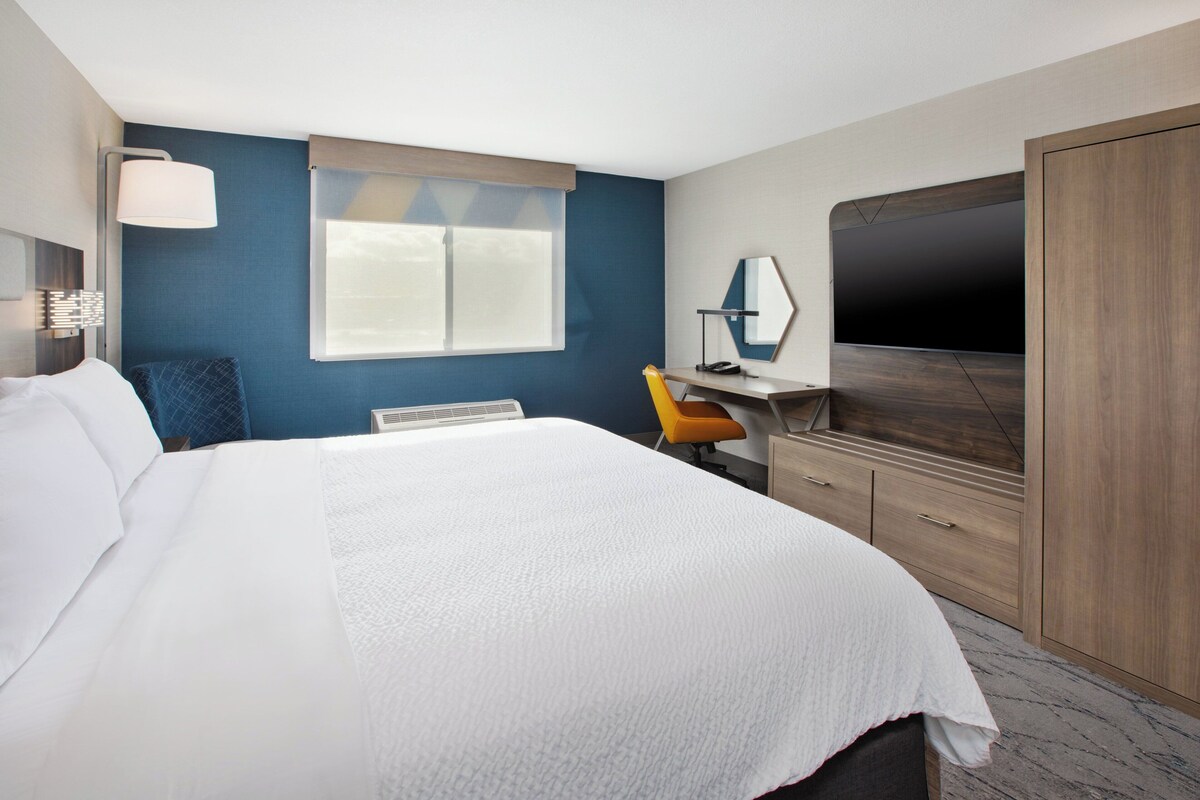 A hotel room with a large bed, a desk with a chair, a TV, and a wardrobe.